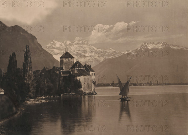 Chillon and the Dent of the Midi, Reproduction of a painting of Chillon Castle on Lake Geneva, with the Dents du Midi in the background, reproduction, photomechanical print, This photomechanical print is part of a cover., inscription: 'Edition Photoglob. 2464. Chillon and the Dent of the Midi.', cliché maker: anonymous, publisher: Photoglob & Co., Kilchberg, 1895 - 1910, photographer, pasteboard, materials by function, paper, varnish, collotype, varnishing, height 209 mm x width 270 mm, The print has been treated with varnish to imitate craquelé., lake, castle, mountains, Lake Geneva, Montreux, Chillon Castle, A large stone castle with steep roofs and a central tower sits on a rocky shoreline surrounded by tall, narrow trees, with dark foliage extending down to calm water that reflects the buildings and trees; a small sailboat with two triangular sails floats near the castle, its reflection visible in the water, while distant low buildings and a small pointed tower line the far shore; ...