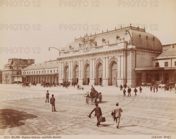 View of Milan station, Italy, Stazione Centrale, architetto Bouchot, Milano, photograph, inscription: '(Diepr. nakomen)', number: '3833.', photographer: Giacomo Brogi (possibly), Milan, publisher: Edizioni Brogi, Florence, after design by Louis-Jules Bouchot, 1864 - 1881, Tuscany, Lombardy, pasteboard, paper, albumen print, height 251 mm x width 331 mm, station, shelter (railway, tramway), exterior, representation of a building, Milano Centrale Station, A wide plaza in front of a large ornate stone building with tall arched doorways and decorative sculpted details along its façade, a curved mansard roof with ornamental urns and a central clock-like round relief, many people walking or standing across the open paved area, several horse-drawn carriages and horses near the building, a few lampposts mounted on curved arms projecting over the plaza, smaller adjacent buildings flanking the main structure, and distant figures and carts near the building edges.