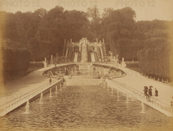 Parc de St. Cloud, La Grande Cascade', Paris, photograph, View of a long symmetrical pond with fountains and some people with umbrellas, parasols?, France, check stamp: 'Photographic ? Company, J.KUHN, PARIS, 220 170174 220, RUE DE RIVOLI', inscription: 'No. 247 PARC de St. Cloud La Grande Cascade X. Phot.', publisher: J. Kühn (publisher), c. 1880 - c. 1900, J. Kühn (publisher), publisher, pasteboard, paper, albumen print, height 222 mm, width 279 mm x width 401 mm, height 304 mm, A wide formal water feature stretches toward a large tiered stone cascade and sculptural terrace set against a densely treed hillside, with parterres and hedges flanking the central axis; stone balustrades line the long reflecting basin, small jets of water arcing into the pool along the sides, and stepped waterfalls descend from the ornate terrace into lower basins; classical statues stand on plinths at the terrace and along the walkways; people in period dress walk or stand on the paths beside the water, so...