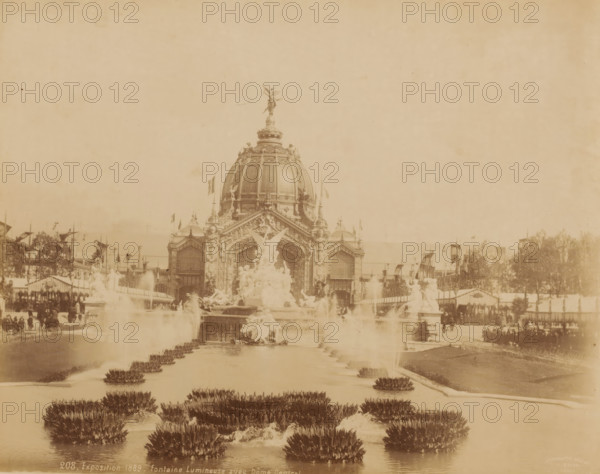 World Exhibition 1889 ('Exposition 1889 - fontaine Lumineuse avec Dôme Central.'), Paris, photograph, France., check stamp: 'Photographic Company, J. Kühn, 220 170174 Rue de Rivoli', inscription: '208, Exposition 1889 - fontaine Lumineuse avec Dôme Central', publisher: J. Kühn (publisher), 1889, photographer, pasteboard, paper, albumen print, albumendruk, height 215 mm, width 275 mm x width 446mm, height 343mm, World's Fair 1889 (Paris), A sepia-toned photograph shows a grand domed building with ornate architectural details and sculptural decorations; a winged statue tops the dome and additional statues and carvings adorn the façade. In front of the building a large decorative fountain complex features multiple sculpted figures and flowing water, with jets and cascades visible. A long reflecting pool or canal stretches toward the foreground, lined with low plant clusters emerging from the water. Flanking the central scene are procession-like rows of flags and banners, temporary structu...