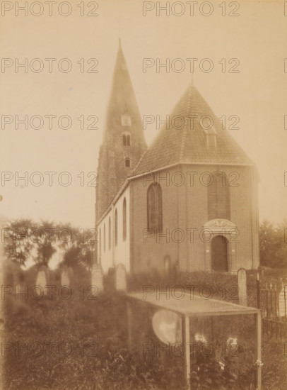 View of the St. Anthony's Church in Surhuizum, photograph, annotation: 'Surhuizen (Friesland), Dutch Reformed Church Sept. 1902, Achtkarspelen', annotation: 'Surhuizum, municipality of Achtkarspelen', photographer: AJM Mulder (possibly), Surhuizum, 1902, AJM Mulder, photographer, Attributed to, paper, pasteboard, albumen print, height 225 mm x width 169 mm, church (exterior), A sepia-toned photograph showing a brick church with a steep tiled roof and a tall pointed tower rising behind it, arched windows along the side of the building, an arched doorway with decorative stonework above it, rows of upright headstones in front of the church, a low metal fence section, trees in the background, and a rectangular glass-topped case or display box in the foreground standing on slender legs with flowers visible beneath it.