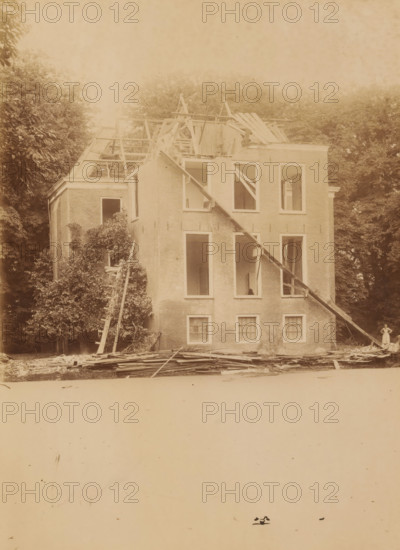Dekema State in Weidum during the demolition, photograph, annotation: 'Weidum, Weidum, Dekema, gem. Baarderadeel', annotation: 'Weidum (Fr), Dekema State, list 1902', photographer: AJM Mulder (possibly), 1902, Attributed to, paper, pasteboard, albumen print, albumendruk, height 227 mm x width 166 mm, villa, A large brick building with its roof partially removed and wooden rafters exposed stands amid tall trees, the facade showing multiple window openings with some interior floors visible, slanted wooden beams propped against the front, scattered planks and debris piled at the base, a ladder leaning into foliage on one side, and a person standing near the building edge dressed in light clothing.