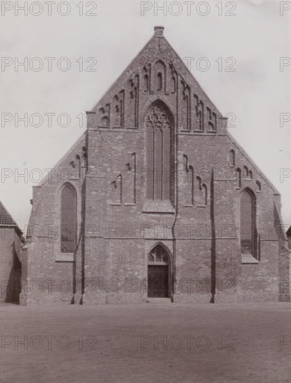 Broerekerk in Bolsward, photograph, annotation: 'Bolsward', annotation: 'Broerekerk, in Bolsward', Bolsward, photographer: AJM Mulder (possibly), c. 1895 - c. 1915, Attributed to, paper, pasteboard, daylight collodion silver print, height 223 mm x width 168 mm, church (exterior), Broerekerk, A large brick building facade with a steep triangular gable and decorative recessed arches, featuring a tall central arched window with tracery and flanking narrow arched windows with lattice panes, a wooden double door set in an arched entrance beneath the central window, buttresses and vertical brick detailing on either side, and a paved open area in front of the building.