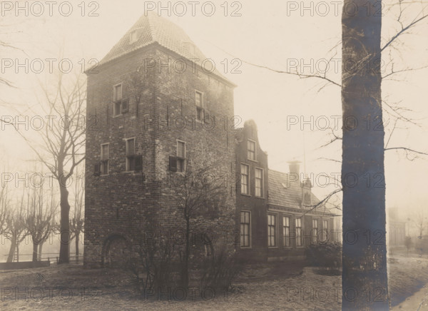 Residential tower Schierstins in Veenwouden, photograph, annotation: 'Dantumadeel, Veenwoude', annotation: 'Veenwouden (Fr), Schierstins restored, 21 Dec 1905', Veenwouden, photographer: AJM Mulder (possibly), 1905, Attributed to, paper, pasteboard, gelatin silver print, height 164 mm x width 224 mm, villa, A tall brick building with a steep tiled roof stands partially obscured by bare trees and a large tree trunk in the foreground; the building shows multiple small windows with shutters and an arched lower opening, and attached to it is a lower structure with larger rectangular windows and a decorative gable and chimney; leafless trees and low shrubs surround the structures and the scene is shrouded in a soft, pale light.