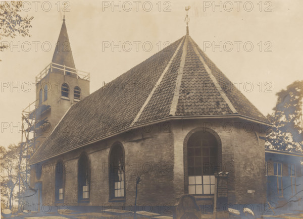Nicolaaskerk in Midlum, photograph, annotation: 'Midlum bij Franeker (Fr), Ned Herv Kerk, oct 1907', annotation: 'Franekeradeel, Midlum', Midlum, photographer: AJM Mulder (possibly), 1907, Attributed to, paper, pasteboard, gelatin silver print, developing gelatin silver print, height 162 mm x width 222 mm, church (exterior), Nicolaaskerk (Midlum), A weathered building with a steep tiled roof and a conical tower is shown, the roof displaying rows of dark, textured tiles and lighter ridgelines, capped by a small ornamental finial; a square bell tower with arched openings and a pointed spire rises beside it, with wooden scaffolding attached to one side; the stone exterior of the building has tall arched windows with dark frames and panes, and a rounded arch above a larger window; nearby trees and foliage frame parts of the scene, and the image has an aged, sepia-toned appearance.