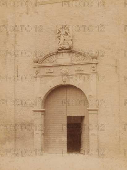 Entrance to the Westerkerk in Harlingen, shortly before its demolition in 1896, photograph, annotation: 'Entrance Westerkerk Harlingen (Fr), July 1896', annotation: 'Harlingen', Harlingen, photographer: AJM Mulder (possibly), 1896, Attributed to, paper, pasteboard, albumen print, height 227 mm x width 174 mm, parts of church exterior and annexes: portal, A large arched doorway set into a brick wall is visible, with heavy wooden doors studded with metal rivets and one door slightly open revealing a dark interior; above the arch is an ornate stone lintel featuring decorative scrollwork, sculpted floral motifs, a central carved face, and a sculpted figure holding a staff standing on a pedestal flanked by carved elements, with carved ornamental details on the pilasters beside the arch and the surrounding brickwork showing regular horizontal courses.