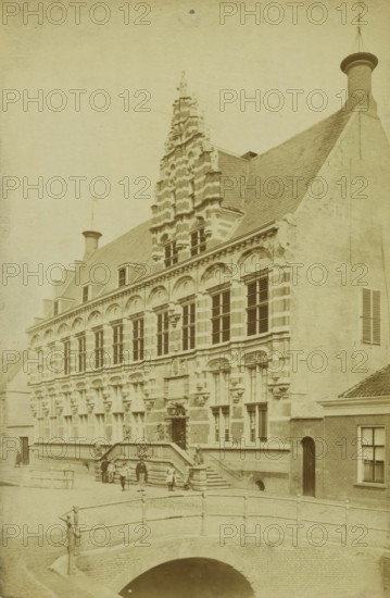 View of the chancery in Leeuwarden, photograph, inscription: '9 Leeuwarden sic. Nieuwe Stad', Leeuwarden, 1860 - 1900, photographer, paper, albumen print, height 182 mm x width 120 mm, façade (of house or building), A large historic stone building with ornate vertical facade details and rows of tall windows stands behind a short flight of steps leading to an entrance; the roof is steep and tiled with chimneys and decorative gables rising above, including a stepped central tower element with layered stonework, and adjacent plain wall sections with shuttered windows; in front of the building a stone balustraded bridge crosses a dark arched waterway, and several small figures and a few people stand or sit on the steps and near the bridge; the scene is rendered in a sepia-toned, aged photographic style.