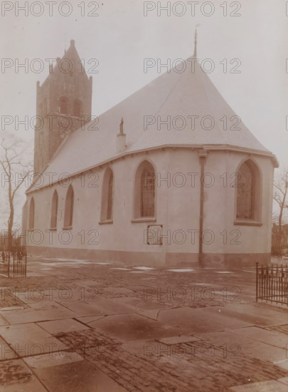 St. John the Baptist Church in Huizum, photograph, annotation: 'Dutch Reformed Church with tower in Huizum (Fr) Jan 1911, Leeuwarderadeel', Huizum, photographer: AJM Mulder (possibly), 1911, Attributed to, paper, pasteboard, daylight collodion silver print, height 224 mm x width 163 mm, church (exterior), A pale stone building with a steep shingled roof and a square tower rising at one end fills the frame, showing arched windows set into smooth walls and a rain gutter running down a corner, a small statue on a pedestal protruding from the roofline, leafless trees visible behind and to the sides, and a paved foreground of worn rectangular stones leading up to the building.