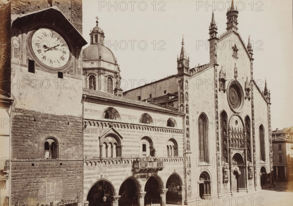 Church with dome and bell tower, Italy ?, photograph, c. 1880 - c. 1900, photographer, paper, albumen print, height 185 mm, width 251 mm, A wide sepia-toned photograph of a historic stone façade showing ornate architectural details, including a large round clock with Roman numerals set under a projecting hood on a tower at the left, a domed structure with windows and decorative columns rising behind the central portion, and a grand church front on the right with tall pointed spires, sculpted niches, a large circular rose window, arched doorways, and rows of carved figures and reliefs along the vertical edges; the lower level features a series of striped stone arches forming a loggia with small balconies and shuttered arched windows above, textured masonry walls, and a street-level view with shadows cast across the ground.