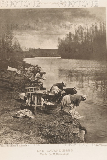 Les lavandières, Women doing laundry on the banks of a river, page, photomechanical print, photographer: M. Mittenhof, France, cliché maker: Rougeron, Vignerot et Cie, printer (person): Chardon-Wittmann (possibly), c. 1883 - in or before 1893, printer (person), paper, photoaquatint, height 150 mm x width 120 mm, river, laundering, A sepia-toned scene shows a riverbank with several women kneeling and bending over near the water, washing textiles in wooden tubs and basins; some garments and cloths lie on the ground and are draped over small wooden wringers and carts nearby. The river occupies the right side of the image, its surface reflecting the overcast sky. Bare trees and dense foliage line the far bank, extending toward the horizon, while the near bank is grassy and uneven with scattered laundry tools and wicker baskets. The overall atmosphere is quiet and focused on the washing activity along the shoreline.