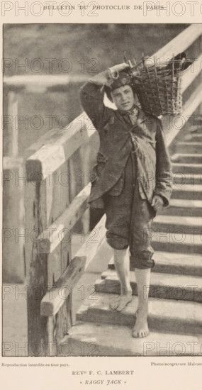 Boy with a basket on his shoulder walking down a staircase, Raggy Jack, page, photomechanical print, inscription: 'Bulletin du Photoclub de Paris', inscription: 'Reproduction interdite en tous pays.', photographer: FC Lambert, cliché maker: Jean Malvaux, c. 1888 - in or before 1893, paper, autotypie, height 180 mm x width 108 mm, youth, adolescent, carrying something in basket, bag, rucksack, flight of steps, A sepia-toned photograph showing a barefoot young man standing on wooden steps beside a railing, wearing rolled-up trousers and a worn jacket, with a patterned scarf around his neck and a cap on his head, holding a woven basket balanced on his shoulder while one hand rests on his head and the other hangs by his side, with the wooden railing and steps forming strong diagonal lines in the composition.
