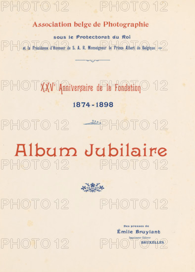 XXVe anniversaire de la fondation, 1874-1898 : album jubilaire, book, date: 'July 1985', number: '1000', 1898, textile materials, paper, linen (material), transparent paper, printing, autotype, height 288 mm x width 227mm x thickness 18mm, A cream-colored page with small scattered brown spots and a large decorative heading in a reddish-brown serif type near the top, a smaller line of dark blue ornate type above it and another line of dark blue type centered below, a small blue decorative flourish between lines, a larger reddish-brown title in the middle of the page, a small blue floral ornament beneath it, and a block of small dark blue type near the lower right portion of the page.