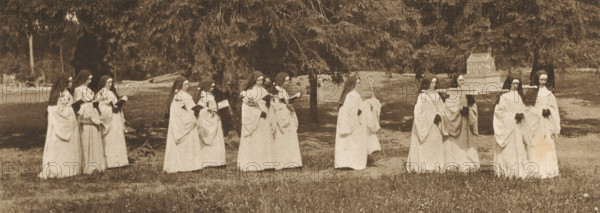 Les Nonnes, Group of nuns, four of whom carry a reliquary, page, photomechanical print, inscription: 'Association belge de photographie 1899.', photographer: Alexandre, cliché maker: Meisenbach, Riffarth & Cie., Berlin, c. 1894 - in or before 1899-02, paper, photoaquatint, height 75 mm x width 198 mm, nun(s), relics (and reliquaries), A sepia-toned outdoor scene shows a line of women in long light-colored robes and dark head coverings walking across a grassy area with trees in the background; several carry small books or bouquets, one holds a staff, and a group near the right carries a decorative box on a platform, while the foreground shows short grass and scattered small flowers.
