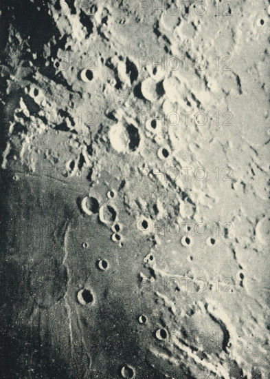 Moon landscape with a map with some craters, page, photomechanical print, tracing, inscription: 'Photographie lunaire obtenue à l'observatoire de Paris, SUD, OUEST, EST, NORD', maker: Loewy et Puiseux, Observatoire de Paris, c. 1891 - in or before 1896, Loewy et Puiseux, Paris, paper, autotypie, height 157 mm x width 113 mm, with map on tracing paper that can be placed over the print., surface of the moon, Moon, A textured surface covered in circular depressions of varying sizes, with raised rims and shadowed interiors, appearing in a grainy monochrome palette; irregular ridges and rough patches surround the depressions, creating a pitted, uneven landscape with contrasts between lighter raised areas and darker recessed zones.