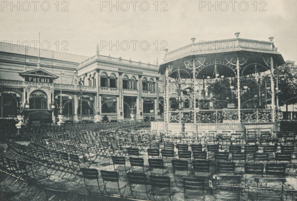 Pailas des fêtes, View of a kiosk in front of Palais des fêtes during the 1894 World Exhibition in Antwerp, photomechanical print, Part of a cover with 49 plates., inscription: 'Exposition Universelle D'Anvers 1894', photographer: Charles Bernhoeft, Antwerp, cliché maker: Charles Bernhoeft, Luxembourg (city), c. 1894, Charles Bernhoeft, photographer, cliché maker, printer (person), paper, collotype, photoprint, height 154 mm x width 222 mm, civic architecture, edifices, dwellings, world fair, world exhibition, World Exhibition 1894 (Antwerp), Period, 1894, A large outdoor scene showing rows of folding chairs arranged across a paved area in front of an ornate raised bandstand with decorative railings, arched supports, and hanging globe lamps, positioned to the right; to the left and center is a two-story classical building with arched windows, columns, ornamental cornices, and a pavilion entrance topped by a triangular pediment; lamp posts and decorative streetlights are visible near th...