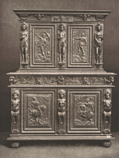 16th century French wooden cabinet, at the 1877 Exposition Rétrospective in Lyon, France, page, photomechanical print, inscription: 'EXPOSITION RÉTROSPECTIVE DE LYON, PAR JB GIRAUD.', number: 'PL. XLII.', inscription: 'ARMOIRE, FRANCE_XVIe SIÈCLE, COLLECTION DE Mme Vve DARDEL.', Lyon, cliché maker: Dujardin, printer (person): Imprimerie Eudes, Paris, 1877 - in or before 1880, photographer, printer (person), paper, photoaquatint, height 252 mm x width 191 mm, ornamental cupboard (wood and other phytogenic material), A tall carved wooden cabinet with ornate panels and sculpted figures, shown straight-on against a plain background, featuring a top cornice with decorative molding and small winged faces, a central section with three framed relief panels depicting human figures in dynamic poses and vertical carved caryatid-like figures flanking the panels, a middle frieze with assorted carved motifs and small faces, and lower doors with framed relief scenes showing mounted figures and flowin...