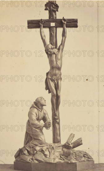 Palm wood crucifix from the collection of CJ Vervloet in Brussels, displayed at an exhibition on religious objects from the Middle Ages and Renaissance in 1864 in Mechelen, photograph, page, number: '9', photographer: Joseph Maes, Mechelen, 1864, paper, albumen print, height 251 mm x width 153 mm, altarcross, crucifix, piece of sculpture, reproduction of a piece of sculpture (wood, eg: panel, arts), Period, A monochrome photograph of a sculpture showing a crucified male figure on a wooden cross with his head bowed and a cloth around his waist, his arms outstretched and hands nailed to the crossbeam; below him a robed kneeling man looks upward with clasped hands, positioned on a rocky base strewn with sacks and a string of beads; a skull rests near broken wooden fragments at the base; the scene is framed against a plain background.