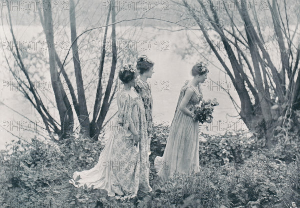 Landscape with three women with flowers in their hair, page, photomechanical print, photographer: Constant Puyo, cliché maker: Jean Malvaux, Brussels, c. 1895 - in or before 1900, paper, autotype, height 154 mm x width 215 mm, flowers, landscapes, adult woman (three persons), Three women in long flowing dresses stand in a natural setting among tall bare tree trunks and low foliage, viewed from the side with their profiles visible; two stand close together while the third is slightly ahead holding a bouquet of flowers, each with hair styled up and small flower adornments, and the scene has a soft, muted monochrome tone.