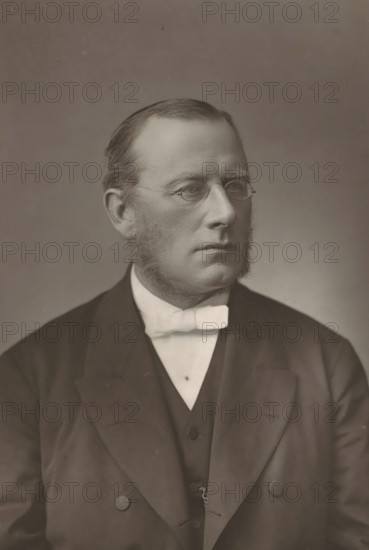 Portrait of Edmond Warre, The Rev. Dr. Warre, page, photomechanical print, inscription: '57 & 61, Elbury Street, London.', photographer: Downey, William & Daniel, London, cliché maker: anonymous, c. 1880 - in or before 1890, paper, Woodburytype, height 141 mm x width 95 mm, Person, Edmond Warre, university organization, A sepia-toned portrait of a man shown from the chest up wearing a dark suit jacket over a dark vest and a light-colored shirt with a light bow tie; he has short, neatly combed hair, full sideburns, and small round eyeglasses, and his expression is neutral while he looks slightly to the side against a plain background.