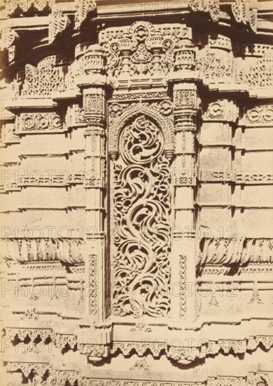 Decoration on the base of a minaret of the Rani Rupamati Mosque in Ahmedabad, The Queen's Mosque in Mirzapoor.- Niche in lower part of base of Northern Minaret, photograph, page, number: '32.', photographer: Thomas Biggs, Ahmedabad (city), c. 1856 - in or before 1866, Thomas Biggs, photographer, Gujarat, paper, albumen print, height 189 mm x width 136 mm, temple, shrine, Islam, Mohammedanism, base (, column, pillar), ornamenting, decorating, applied arts, Rani Rupamati Mosque, A close-up of a carved stone facade showing an ornate vertical panel with swirling, organic openwork patterns framed by carved pilasters, flanked by horizontal bands and rectangular blocks with repetitive carved motifs, rosettes, and decorative borders, with layered cornices and small projecting brackets topped by a carved entablature and additional lattice-like panels.