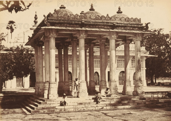 Sirkhej.- The Pavilion, and the Tomb of Gunj Buksh, Pavilion and the tomb of Ahmed Khattu Ganj Baksh at Sarkhej Roza near Ahmedabad, photograph, page, number: '43.', photographer: Thomas Biggs, Sarkhej Roza, c. 1856 - in or before 1866, Gujarat, paper, albumen print, height 136 mm x width 187 mm, grave, tomb, A stone pavilion with a raised platform and a colonnade of tall square pillars supports an ornate flat roof topped by multiple domes and decorative finials, with carved cornices and scalloped edging along the roofline; steps lead up to the platform and a few seated and standing figures in traditional clothing are on and near the steps; behind the pavilion a building with arched openings and patterned window screens is visible, and trees frame parts of the scene.