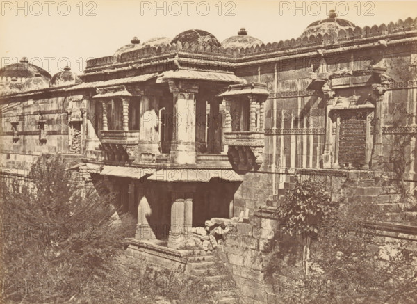 Sirkhej.- Porch in the Southern Colonnade of the Mosque, View of a portal of a mosque at Sarkhej Roza near Ahmedabad, photograph, page, inscription: 'O', number: '49.', photographer: Thomas Biggs, Sarkhej Roza, c. 1856 - in or before 1866, Gujarat, paper, albumen print, height 135 mm x width 188 mm, temple, shrine, Islam, Mohammedanism, parts of church exterior and annexes: porch, A sepia-toned photograph of an ornate stone building showing carved columns, decorative cornices, and domed rooftop structures with finials, with carved brackets supporting projecting balconies and a section of a wall punctuated by a recessed opening filled with stacked stones, surrounded by shrubbery and rough stone steps and rubble at the base.