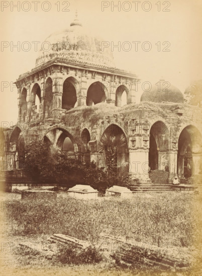 Butwa, - The Tomb of Kootub-i-Alum, Tomb of Kootub-i-Alum in Batwa near Ahmedabad, photograph, page, number: '60.', photographer: Thomas Biggs, Ahmedabad (district), c. 1856 - in or before 1866, Gujarat, paper, albumen print, height 202 mm x width 148 mm, Person, Kootub-i-Alum, grave, tomb, A sepia-toned photograph of an old stone building with large rounded domes and multiple arched openings, showing weathered and textured stonework, carved details around the arches, and vegetation growing on and around the structure; a foreground of grassy ground with scattered stone slabs and low tomb-like structures sits before the building, and a single person wearing light clothing and a hat sits on steps near one of the arches.