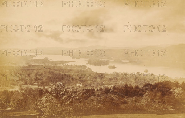 View over Windermere, Winander Mere, from Elleray, looking south, photograph, page, photographer: Garnett & Sproat, Lake District, c. 1857 - c. 1867, paper, albumen print, height 106 mm x width 163 mm, lake, Windermere, A wide sepia-toned landscape showing a lake with several small islands and peninsulas surrounded by rolling hills and tree-covered terrain, a foreground of dense trees and foliage, scattered buildings partially visible among the trees, a calm water surface reflecting the sky, distant layered hills fading into the background, and a cloudy sky with soft, diffuse light.