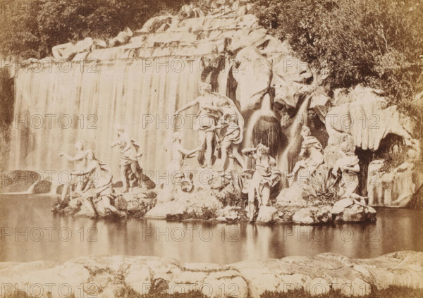 View of a fountain with women fleeing, photograph, page, c. 1850 - in or before 1860, photographer, paper, albumen print, height 96 mm x width 135 mm, monumental adornments (in city), A sepia-toned scene showing a cascading waterfall behind a rocky formation populated by multiple sculpted figures, with flowing water spilling into a calm reflecting pool in the foreground; the stone figures are arranged on various rock ledges and outcrops, many posed in dynamic gestures with draped garments, some leaning or seated, and a few standing near the water's edge; large rounded boulders and carved rock faces frame smaller streams of water descending beside the main fall, while vegetation and trees appear behind and around the rocky area, and the still water in front reflects parts of the rocks and figures.