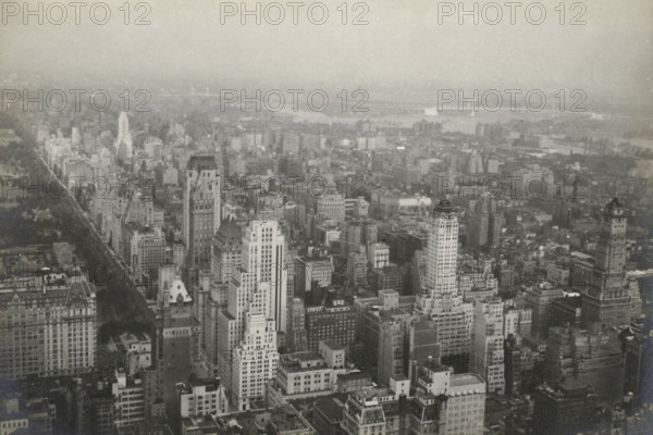 New York from RCA building uptown, New York seen from the RCA Building (now GE Building), part of the Rockefeller Center, United States, photograph, title: 'NEW YORK FROM, RCA BUILDING UPTOWN.', photographer: attributed to Wouter Cool, United States of America, 1936, North America, Attributed to, pasteboard, paper, gelatin silver print, developing gelatin silver print, height 157 mm x width 231 mm, height 315 mm x width 286 mm, city-view, and landscape with man-made constructions, skyscraper, A wide aerial view of a dense cityscape in grayscale showing many tall buildings of varying architectural styles and heights clustered close together, with streets and rooftops visible between them; a long tree-lined avenue extends from the foreground toward the left side, bordered by rows of buildings; distant low-rise areas and a waterway with bridges span the upper part of the scene, fading into a hazy sky above.