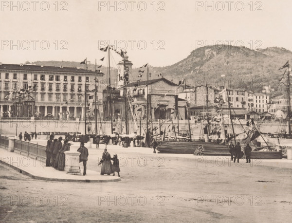 Le port, View of the harbor of Nice, page, photomechanical print, inscription: '35 Boulevard des Capucines Paris', inscription: 'Nice', photographer: Otto van Bosch, Nice, photographer: Paul Boyer (1861-1908), cliché maker: Dujardin, printer (person): Chardon-Wittmann, c. 1888 - in or before 1890, printer (person), Provence-Alpes-Côte d'Azur, paper, photoaquatint, height 186 mm x width 233 mm, Print after page 135., harbour, A waterfront scene showing a promenade with a stone balustrade and lampposts, people in period clothing walking and standing in groups, and a cluster of masts and rigging from moored sailing vessels decorated with flags and pennants. Behind the boats a long multi-story building with many windows and balconies faces the water, alongside a clock tower and additional smaller stone buildings. Stacked timber and cargo are visible near the quayside, and hills covered in vegetation rise in the background. The image has a monochrome, sepia-toned appearance.