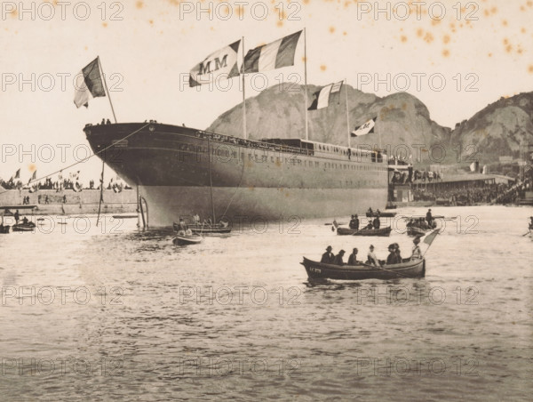 Le Polynésien à flot, Le Polynésien off the coast at La Ciotat, page, photomechanical print, inscription: '35 Boulevard des Capucines Paris', inscription: 'La Ciotat', photographer: Otto van Bosch, La Ciotat, photographer: Paul Boyer (1861-1908), cliché maker: Dujardin, printer (person): Chardon-Wittmann, c. 1888 - in or before 1890, printer (person), Provence-Alpes-Côte d'Azur, paper, photoaquatint, height 185 mm x width 231 mm, Print after page 46., harbour, ships (in general), A large ship is moored near a pier with multiple flags flying from its masts, its hull dominating the left and center of the scene and casting reflections on the water; several small rowboats with people are scattered on the water in front of the ship, and a crowd of people lines the pier along the shore; rocky hills rise in the background behind the pier and ship, and the sky above is light with scattered darker spots.