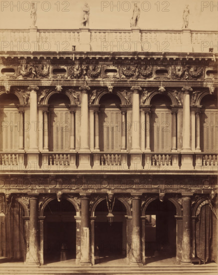 Palace opposite the Doge's Palace in Venice, photograph, photographer: attributed to Carlo Naya, c. 1850 - c. 1900, Carlo Naya, photographer, Attributed to, paper, pasteboard, albumen print, height 352 mm x width 270 mm, height 650 mm x width 270 mm, Venice, A multi-level stone façade with arched openings and tall columns, decorative capitals and balustrades, shuttered windows behind the arches on the upper level, sculpted reliefs and garlands in the horizontal frieze, carved human figures and heads integrated into the ornamentation, statues standing along the roofline, a hanging lantern beneath one of the arches, heavy curtains or drapery at the sides of the lower arches, weathered surfaces and patches of darker staining on the stone.