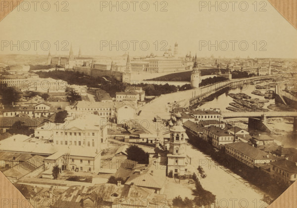 Moscow. Face of Kremlin, photograph, Russia, 1850 - 1900, photographer, paper, albumen print, height 100 mm x width 150 mm, height 220 mm x width 160 mm, Moscow, A sepia aerial view of a riverside cityscape showing a long fortified complex with towers and domes along an embankment, a river with multiple moored barges and boats, a roadway running beside the river and crossing a bridge, rows of low buildings with pitched roofs and courtyards in the foreground, a tall bell tower with ornamental domes rising above nearby structures, tree-lined banks and open paved areas, and distant spires and rooftops fading into the horizon.