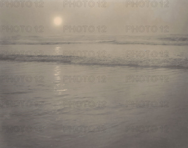 Seascape, photograph, photographer: Rudolf Eickemeyer, 1900 - 1906, pasteboard, paper, platinum process, height 184 mm x width 234 mm, height 278 mm x width 432 mm, ocean, A muted seascape with a pale disc of light low in a hazy sky reflecting as a vertical shimmer on calm water, gentle wavelets and foamy surf stretching across the midground, and smooth rippled water in the foreground, all rendered in soft gray and beige tones.