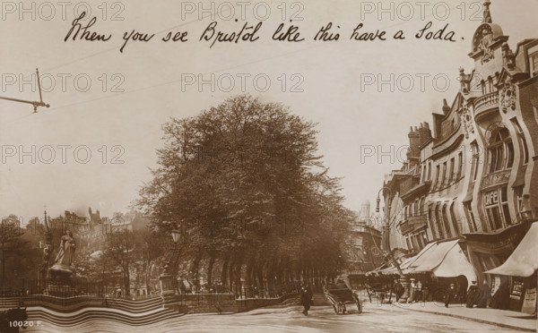 When you see Bristol like this have a Soda, Rotary 'Grotesque' Series, photograph, picture postcard, Bristol, publisher: Rotary Photographic Co., London, 1905 - 1920, photographer, paper, baryta paper, daylight gelatin silver print, height 85 mm x width 136 mm, drunkenness, street (city(-scape) with figures, staffage), A sepia-toned street scene shows a row of tall leafy trees along a sidewalk, a statue on a pedestal within a fenced area to the left, and ornate multi-story buildings with decorative facades and awnings lining the right side; people in period clothing stand and walk along the street, a handcart is visible near the center, street lamps and railings appear along the avenue, and overhead lines cross the pale sky.