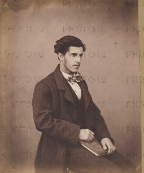 Portrait of an unknown seated young man with a checkered bow tie, with a book in his hand, photograph, photographer: attributed to Franz Hanfstaengl, Germany, c. 1855 - c. 1860, Attributed to, paper, salted paper print, salt print, height 189 mm x width 154 mm, height 238 mm x width 239 mm, anonymous historical person portrayed, A young man is seated against a plain background, shown from the waist up and turned slightly to his right; he has dark, wavy hair styled away from his face and faint sideburns, a straight nose, and a neutral expression with his gaze directed off to the right. He wears a dark coat over a fitted vest and a light-colored shirt with a patterned bow tied at the collar. One hand rests on his lap while the other holds a rectangular object with a patterned cover. The photograph has a sepia tone and shows slight aging marks and small spots on the background and edges.