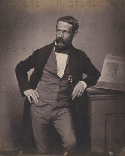 Portrait of an unknown man with glasses and beard, photograph, inscription: 'Ingammikonz', photographer: attributed to Franz Hanfstaengl, Germany, c. 1855 - c. 1860, Attributed to, paper, salted paper print, salt print, height 205 mm x width 154 mm, height 238 mm x width 239 mm, anonymous historical person depicted, A seated man in formal attire with a beard and mustache leans against a wooden pedestal while holding a cane, wearing a dark jacket over a waistcoat and a white shirt with a bow tie, one hand resting on his hip and the other on the pedestal where an open book is placed, the background is plain and the image has a muted, sepia tone.