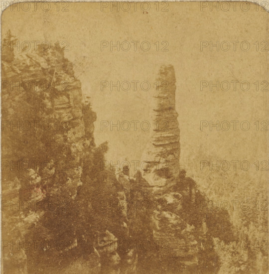 View of the rock formation Malý Pravcický kužel in the Elbe Sandstone Mountains, Czech Republic, Der Prebischkegel, Views and landscapes in Europe, Africa and Asia, Geographical Sculpture Gallery, collected by MJ Broekhuijsen, Headmaster of a school in Amsterdam, stereograph, Numbered 16. in the lower right corner of the photo, annotation: 'A steep rock in the Elbe Sandstone Mountains, almost as high as the Westertoren in Amsterdam.', Elbe Sandstone Mountains, publisher: Merkelbach & Co., Amsterdam, compiler (person in literature): Martien Johan Broekhuijsen, c. 1905, photographer, compiler (person in literature), pasteboard, paper, albumen print, height 89 mm x width 178 mm, Part of a group of 52 stereophotos used in primary education as a supplement to school charts. The entire series consisted of 274 items in 10 categories (A to K)., rock-formations, Malý Pravcický kužel, A vertically oriented, aged paper surface with a mottled brown and tan texture showing darker stains and faded a...