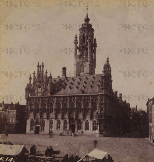 View of the town hall of Middelburg, Town Hall in Middelburg, Views and landscapes in Europe, Africa and Asia, Geographical Sculpture Gallery, collected by MJ Broekhuijsen, Headmaster of a school in Amsterdam, stereograph, Numbered lower left of photo: F.14., Middelburg, publisher: Merkelbach & Co., Amsterdam, compiler (person in literature): Martien Johan Broekhuijsen, c. 1905, photographer, compiler (person in literature), pasteboard, paper, albumen print, height 88 mm x width 178 mm, Part of a group of 52 stereophotos used in primary education as a supplement to school charts. The entire series consisted of 274 numbers in 10 categories (A to K)., town hall, A large ornate stone building with Gothic architectural details occupies the center, featuring a steep roof punctuated by dormer windows and decorative pinnacles, a tall central tower with an onion-shaped spire and smaller turrets, and a facade of arched windows and sculpted stonework; in front of the building there is an open pa...