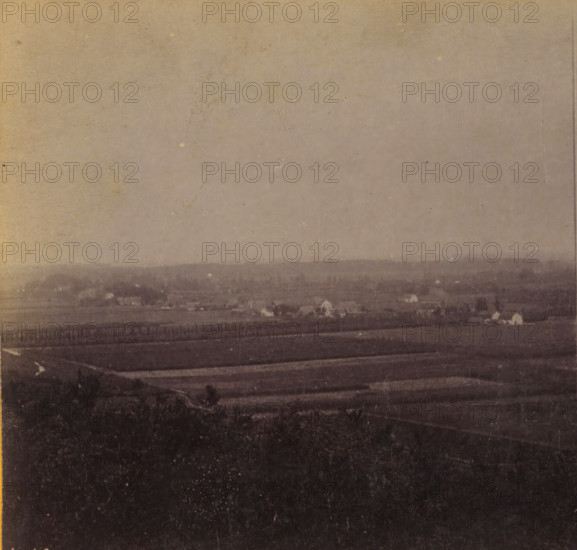 View of Leersum from the Darthuizerberg, View of Leersum, Views and landscapes in Europe, Africa and Asia, Geographical Sculpture Gallery, collected by MJ Broekhuijsen, Headmaster of a school in Amsterdam, stereograph, Numbered lower left of photo: A.18., annotation: 'taken from the Darthuizerberg (Nellenstein tomb). Arable land at the foot of the mountain.', publisher: Merkelbach & Co., Amsterdam, compiler (person in literature): Martien Johan Broekhuijsen, c. 1905, photographer, compiler (person in literature), pasteboard, paper, albumen print, height 87 mm x width 177 mm, Part of a group of 52 stereophotos used in primary education as a supplement to school charts. The entire series consisted of 274 numbers in 10 categories (A to K)., village, Leersum, A faded, grainy landscape photograph showing a wide expanse of land with layered horizontal bands of darker and lighter tones, a distant low ridge or treeline near the middle of the image, scattered small bright spots that resemble is...