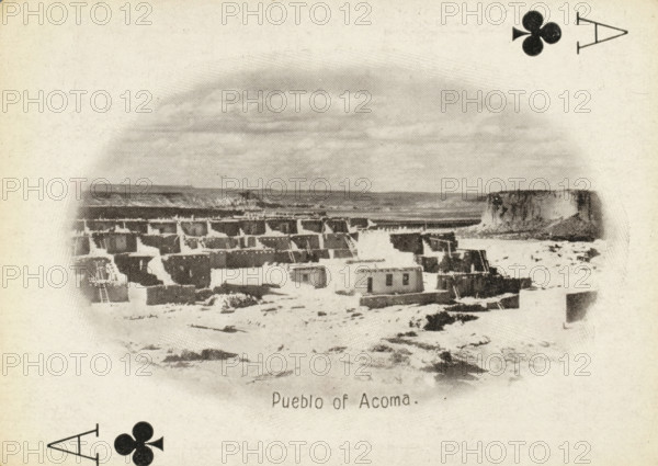 Pueblo of Acoma, Ace of clubs with a face on Acoma Pueblo, New Mexico, photograph, playing card, Playing card from a box with 53 playing cards with autotype images of Native Americans. Contents include a complete set of playing cards including joker., photographer: Adam Clark Vroman, United States of America, publisher: Lazarus & Melzer, Los Angeles (city), c. 1900, North America, paper, autotypie, height 88 mm x width 63 mm, A grainy black and white scene shows a cluster of low, rectangular adobe buildings arranged on a flat, rocky terrain with stepped terraces and flat roofs, some structures appearing partially ruined, with a wide, flat-topped mesa rising in the background and an expanse of sky above; decorative club suit symbols appear near the corners of the image.