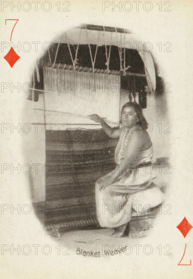 Blanket Weaver, Seven of Diamonds with woman at loom weaving a blanket, photograph, playing card, Playing card from a box of 53 playing cards with autotype images of Native Americans. The contents include a complete set of playing cards including a joker., photographer: Adam Clark Vroman, United States of America, publisher: Lazarus & Melzer, Los Angeles (city), c. 1900, North America, paper, autotype, height 88 mm x width 63 mm, A seated person wearing a draped garment and a beaded necklace is positioned beside a large vertical loom with threads hanging and woven fabric visible, the person’s arm is extended toward the loom and they are looking toward the viewer, the scene appears within an oval vignette on a textured light background with a red diamond shape near the top left and another near the lower right.