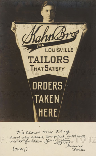 Advertisement for Kahn Bros, Louisville, picture postcard, inscription, United States of America, c. 1930 - c. 1950, photographer, North America, paper, gelatin silver print, developing gelatin silver print, height 138 mm x width 89 mm, Person, Kahn Bros, Kentucky, A sepia-toned photograph of a man seen from the chest up holding a large triangular pennant in front of him, his hands gripping the top corners and his face partially visible above the pennant with short dark hair and a neutral expression; the pennant has alternating light and dark sections with bold graphic lettering and blocky shapes, and there is a lighter rectangular strip across the top edge; below the pennant the image shows a lighter paper area with cursive handwriting and a small parenthetical word, the handwriting slants and fills the space with several lines of flowing script.