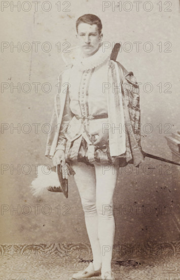 Portrait of Tj.AMA Humalda van Eysinga in costume with hat in hand, album page, photograph, carte-de-visite, This photo is part of an album., inscription: 'J. Goedeljee, Photographer, HRH PRINCE ALEXANDER, of the Netherlands, PRINCE of ORANGE, and HRH, PRINCESS HENDRIK, Hoogewoerd 160, near the Plantage.', name: 'Tj. AMA Humalda, van Eysinga., 93.', photographer: Jan Goedeljee, Leiden, 1860 - 1905, paper, pasteboard, albumen print, albumendruk, height 83 mm x width 52 mm, Person, Tj.AMA Humalda van Eysinga, historical persons, head-gear: top hat, historical costume, A full-length sepia photograph of a person standing in ornate historical costume, wearing a ruffled collar and a decorated robe with patterned trim draped over one shoulder, a buttoned doublet with a belted waist and a short padded skirt, fitted hose, and flat shoes; the person holds a wide-brimmed hat with a large plume in one hand and a sword hangs at the waist and over the shoulder; the background is plain and the floor ...