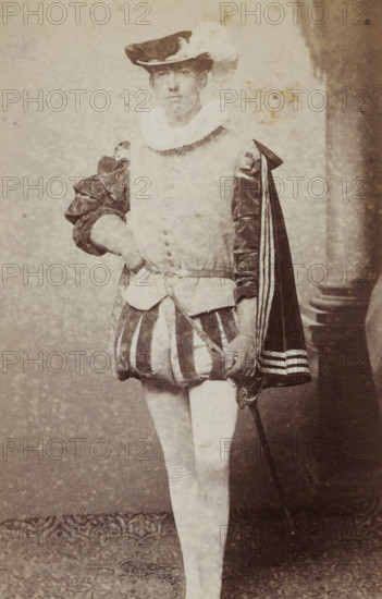 Portrait of a young man in costume with a sword, identified as JAE Rhede van der Kloot, album page, photograph, carte-de-visite, This photo is part of an album., name: 'J. AE. Rhede vd Kloot., 100.', inscription: 'J. Goedeljee, Photographer, HRH PRINCE ALEXANDER, of the Netherlands, PRINCE of ORANGE, and HRH, PRINCESS HENDRIK, Hoogewoerd 160, near the Plantage.', photographer: Jan Goedeljee, Leiden, 1860 - 1905, paper, pasteboard, albumen print, height 83 mm x width 52 mm, historical persons, historical costume, hacking and thrusting weapons: rapier, A faded sepia photograph of a standing person wearing a historical costume with a plumed hat, a ruffled collar, a doublet with decorative buttons, puffed sleeves, a short striped skirt-like garment, fitted hose, and a cape draped over one shoulder; the person has one hand resting on their hip and the other holding a sword at their side; a column and draped backdrop are visible to one side and a patterned floor covering is beneath their fee...