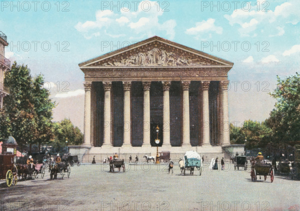 View of La Madeleine in Paris, Paris. - La Madeleine., photograph, page, Part of Photo album with color shots of sights in Paris., Paris, c. 1900 - c. 1930, photographer, pasteboard, paper, autotypie, color autotypie, height 197 mm x width 159 mm, traveling, tourism, prospect of city, town panorama, silhouette of city, church (exterior), street (city(-scape) with figures, staffage), animal traction, animal-drawn vehicle (carriage etc.), Madeleine, A wide stone building with a triangular pediment and a row of tall fluted columns stands centered in the image, its facade featuring sculpted reliefs in the pediment. In front of the building is a broad paved square with a freestanding ornate street clock mounted on a post. Horse-drawn carriages and carts are scattered across the square, with drivers and several pedestrians visible nearby. Trees and leafy foliage frame the scene on both sides, and a pale blue sky with scattered white clouds fills the upper part of the image.
