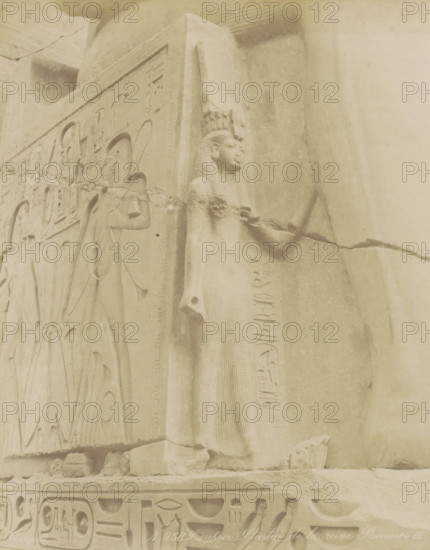 Sculpture of the queen of Pharaoh Ramses II in Luxor, Louksor Statue de la reine Ramses III, photograph, Part of Travel album with 80 photos of Egypt., negative number: '958', photographer: Zangaki, C. & G., Luxor, c. 1870 - c. 1890, North Africa, pasteboard, paper, albumen print, height 275 mm x width 220 mm, Contrary to what the title states on the object, this is Ramses II, piece of sculpture, reproduction of a piece of sculpture, A weathered stone relief showing a standing female figure in profile wearing a tall headdress and a long, textured dress, with braided hair and an arm extended forward holding an object; adjacent carved panels feature other figures in profile and decorative motifs, with bands of carved symbols along the base and side; the surface shows cracks, chips, and worn areas, and the scene is rendered in pale, sandy tones.