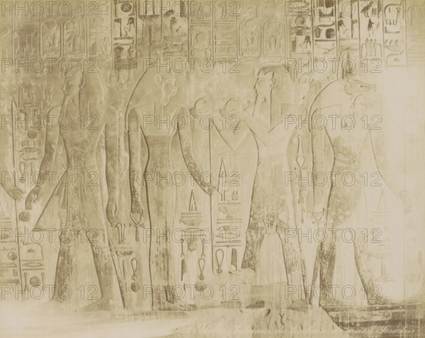 Walls of the burial chamber of Pharaoh Senuseret (Sesostris) in Thebes (former title), Thebes Interior of the tombeau de grand Sesostrio, Tomb of Seti I (KV17) in the Valley of the Kings, Thebes (Luxor), photograph, Part of Travel album with 80 photos of Egypt., negative number: '938', photographer: Zangaki, C. & G., c. 1870 - c. 1890, North Africa, Upper Egypt, pasteboard, paper, albumen print, height 218 mm x width 277 mm, grave, tomb, Luxor, A horizontal stone relief in a pale beige tone shows carved human figures in profile wearing traditional Egyptian headdresses and garments, standing and facing each other across the surface; the figures display elongated limbs and stylized facial features with braided or straight hair, and some hold round objects or ritual implements near their chests while others rest hands by their sides; surrounding the figures are vertical columns of carved symbols and decorative motifs arranged in bands above and between the figures, and the surface shows a...