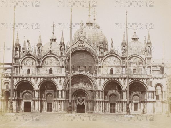 Facade of the Basilica of San Marco and domes in Venice, Venezia - chiesa S. Marco facciata principale, Eglise Saint Marc., photograph, Part of Topographical album of Venice 1881., negative number: '2', check stamp: 'Carlo Ponti Venezia', photographer: Carlo Ponti, Venice, 1860 - 1881, paper, albumen print, height 200 mm x width 260 mm, church (exterior), dome, architecture, Roman Catholic Church, travel, Basilica of San Marco, A large ornate stone facade with multiple arches and domes fills the image, featuring detailed carvings, sculpted figures, and decorative arches above doorways. Several tall slender columns and flagpoles rise in front of the building, intersecting the view of the domes and arches. The upper section shows rounded domes topped with ornamental finials and statues, and triangular gables adorned with relief panels and sculpted figures. The lower section displays arched entrances with carved surrounds, pilasters, and recessed doorways, some with decorative drapery and...